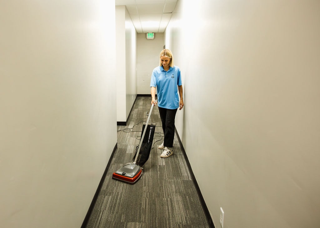 Cleanspace team member vacuuming a long, empty commercial hallway with an upright vacuum