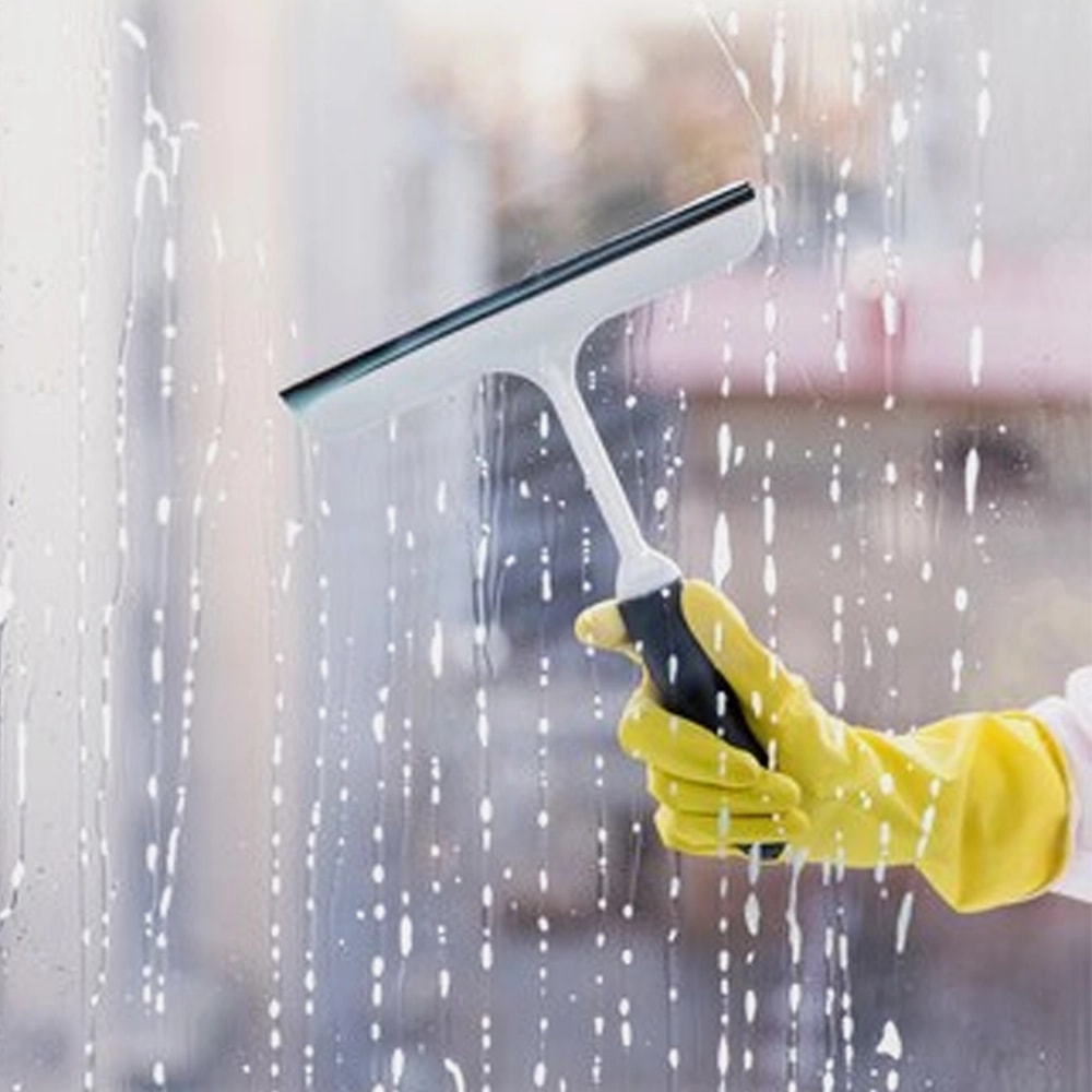 Gloved hand pulling a squeegee across wet glass