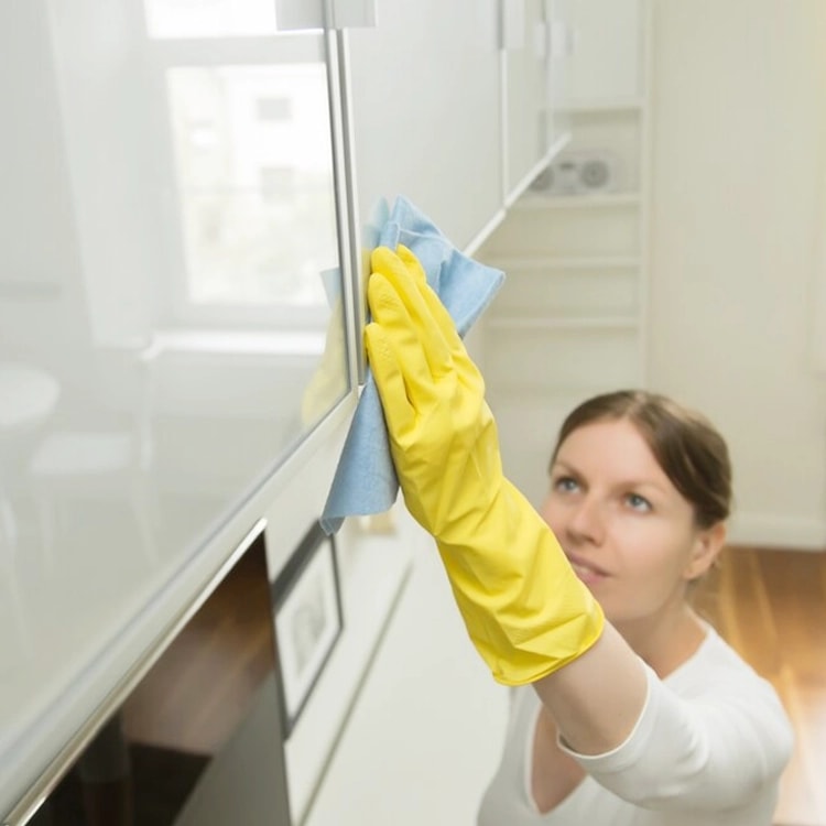 Cleaner in yellow gloves polishing a glossy white surface with a microfiber cloth