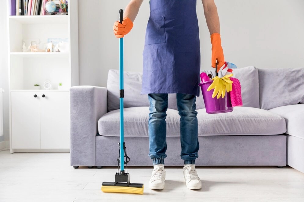 Cleaner holding a mop and a caddy of cleaning supplies in a living room